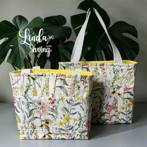 May include: Two floral print tote bags with white handles and yellow lining. The bags feature a variety of colorful flowers and green foliage on a cream background. The bags have exterior pockets and the text "Linda Luvs Saving".