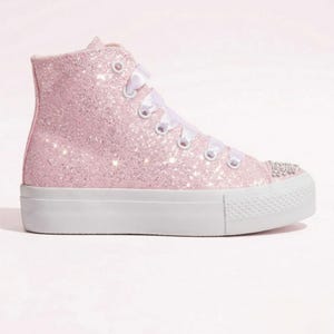 Könnte beinhalten: Rosa Glitzer-High-Top-Sneaker mit weißen Schnürsenkeln und weißer Plateausohle. Die Schuhspitze ist mit kleinen, funkelnden Strasssteinen verziert. Der Schuh hat ein High-Top-Design und ein glitzerndes Finish.