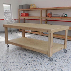 May include: A light-colored wooden workbench with a lower shelf and rolling casters. The workbench is in a workshop setting, with shelving units and tools visible in the background. The workbench measures approximately 60 inches long.