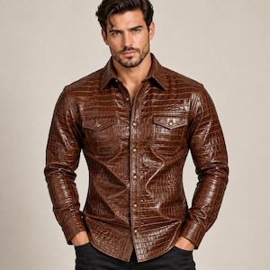 May include: A long-sleeved button-down shirt in a rich brown colour with a textured crocodile skin pattern. The shirt features a classic collar, a front button placket, and two chest pockets with buttoned flaps, providing a structured appearance.
