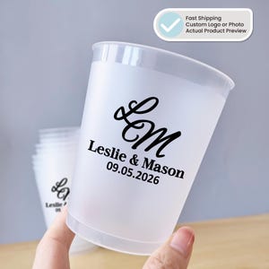 May include: Frosted plastic cups with a custom black design. The design includes the initials "LM", the names "Leslie & Mason", and the date "09.05.2026". The cups are ideal for weddings or events.