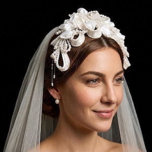 Peut inclure: Coiffe de mariée blanche ornée de fleurs et de perles. La coiffe est ornée de fleurs en tissu, de perles et de brins perlés pendants. Un voile transparent complète le design élégant. Le fond est noir.