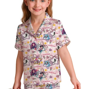 May include: Pink pajama set with a repeating pattern of cartoon characters, stars, and bows. The short-sleeved top and shorts feature the word "HUNTRIX" and are trimmed in pink. The set is made of a soft, silky material.