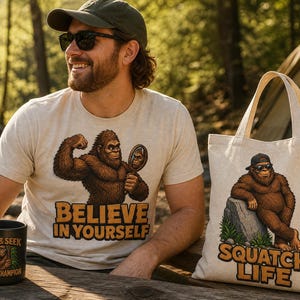 May include: A beige t-shirt featuring a brown Bigfoot holding a mirror with the text BELIEVE IN YOURSELF, a black mug with a Bigfoot graphic and the text HIDE & SEEK WORLD CHAMPION, and a beige tote bag with a Bigfoot graphic and SQUATCH LIFE text.