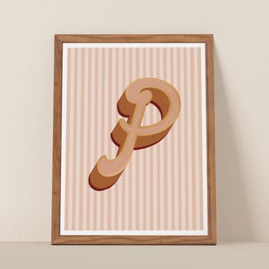 May include: A framed print featuring a stylized letter "P" in a 3D design. The letter is in shades of brown and tan, with a shadow effect. The background has vertical stripes in a light pink color. The frame is made of wood.
