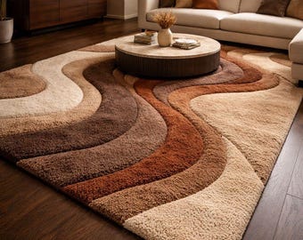 May include: A large, rectangular area rug with a wavy, layered design in shades of beige, brown, and rust. The rug has a plush, textured surface and is placed on a dark wood floor. The rug is a statement piece for a living room.