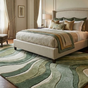 May include: A bedroom scene featuring a large bed with a cream-colored headboard and bedding in shades of green and gold. A patterned rug in green and white tones covers the floor. The room includes a chair, ottoman, and a side table with a lamp.