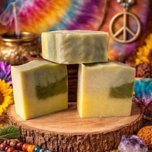 May include: Three rectangular bars of pale green and yellow tallow soap stacked on a circular wooden slice. The soap bars have a smooth, solid texture with visible color variations of light green and cream, showcasing a natural, handcrafted appearance.