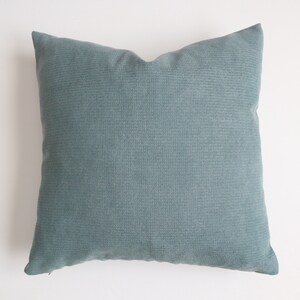 May include: A soft, teal blue throw pillow with a subtle textured fabric. The pillow is square and has a simple design.