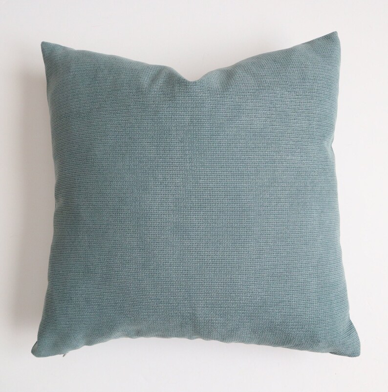 May include: A soft, teal blue throw pillow with a subtle textured fabric. The pillow is square and has a simple design.