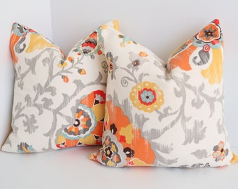 May include: Two decorative throw pillows with a floral pattern in shades of orange, yellow, gray, and blue on a white background.