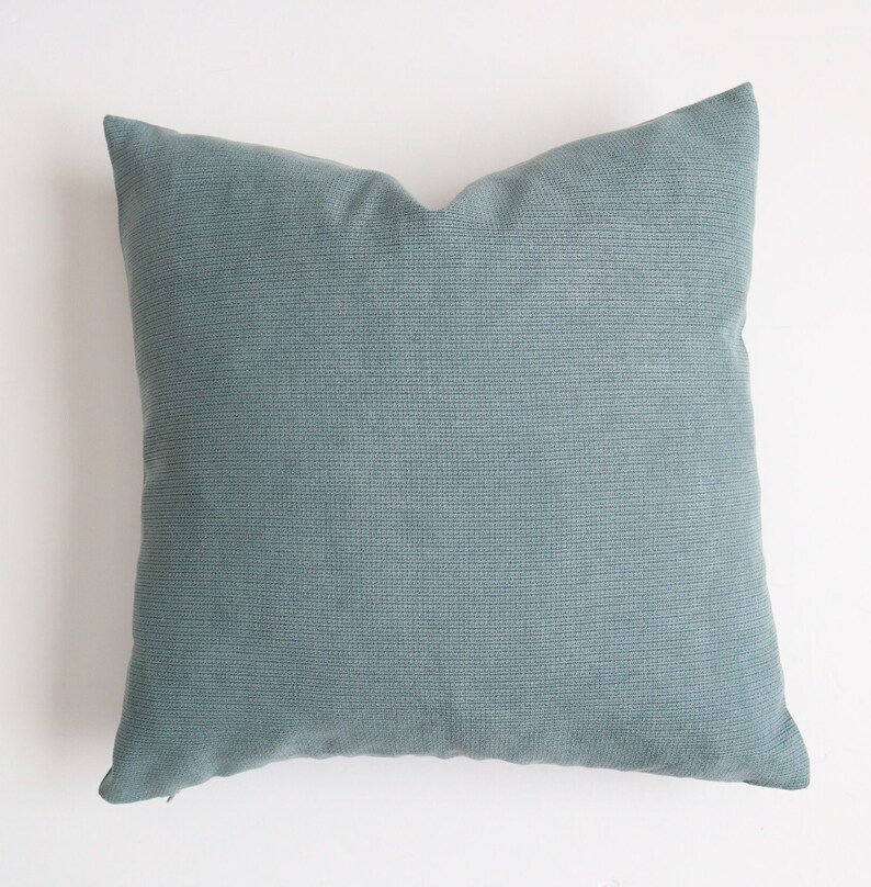 May include: A soft, light blue throw pillow with a subtle textured fabric. The pillow is square and has a zipper closure.