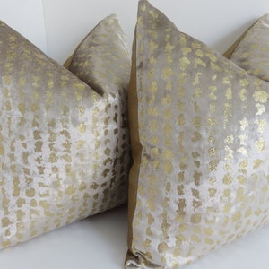 Puede incluir: Dos cojines decorativos con una superficie suave y texturizada. Los cojines son de color beige claro con un patr&oacute;n dorado. Los bordes de los cojines tienen un borde dorado. Los cojines est&aacute;n dise&ntilde;ados para la decoraci&oacute;n del hogar.