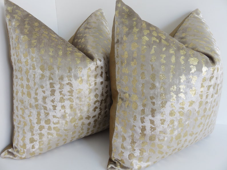 Puede incluir: Dos cojines decorativos con una superficie suave y texturizada. Los cojines son de color beige claro con un patr&oacute;n dorado. Los bordes de los cojines tienen un borde dorado. Los cojines est&aacute;n dise&ntilde;ados para la decoraci&oacute;n del hogar.