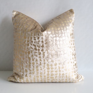 Puede incluir: Un coj&iacute;n decorativo cuadrado con fondo beige y un patr&oacute;n dorado. El patr&oacute;n dorado est&aacute; formado por peque&ntilde;as formas irregulares. El coj&iacute;n tiene una textura suave y aterciopelada, ideal para la decoraci&oacute;n del hogar.