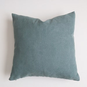May include: A soft, teal blue throw pillow with a subtle textured fabric. The pillow is square and has a zipper closure.