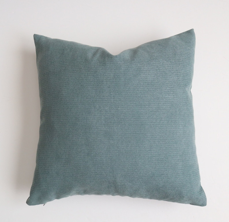 May include: A soft, teal blue throw pillow with a subtle textured fabric. The pillow is square and has a zipper closure.
