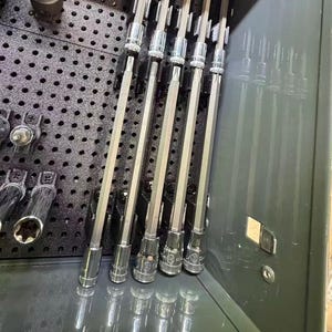 Könnte beinhalten: Eine Sammlung von Metallwerkzeugen, darunter Steckschlüssel und Innensechskant-Bits, ordentlich in einer grauen Werkzeugkiste angeordnet. Die Werkzeuge sind auf einer schwarzen Lochwand und in einer Schublade angeordnet. Das Bild zeigt eine Vielzahl von Größen und Formen.