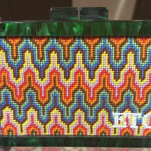 May include: A rectangular clutch bag with a dark green marbled acrylic frame and a clasp closure. The center panel features a multi-colored needlepoint design with a repeating chevron pattern in orange, blue, yellow, and red, including the letters BTQ.