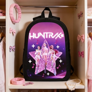 Może przedstawiać: Czarny plecak z grafiką z napisem "HUNTR/X" i trzema postaciami. Projekt zawiera gwiazdę, nuty muzyczne oraz fioletowo-różową kolorystykę. Plecak posiada górny uchwyt i regulowane paski.