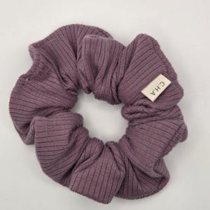 Puede incluir: Una goma para el pelo de color malva hecha de tela acanalada. Una peque&ntilde;a etiqueta rectangular con las letras "C.H.A" est&aacute; cosida en la goma. La goma es circular y parece estar hecha de un material suave.