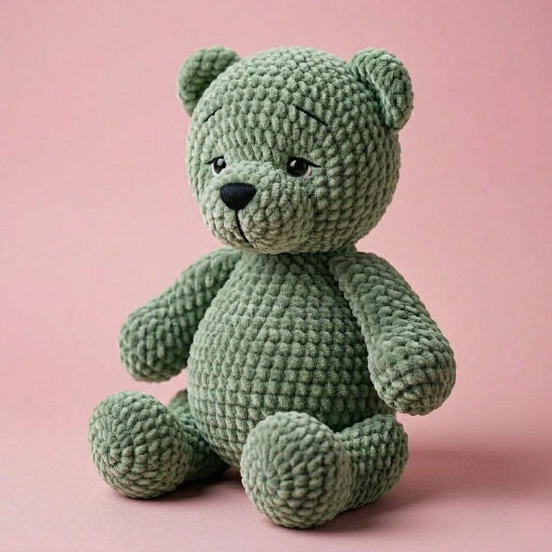 Peut inclure: Un ours en peluche au crochet vert sauge avec un nez noir et des yeux brod&eacute;s. L'ours en peluche est assis sur un fond rose. L'ours a un aspect textur&eacute; et doux. Un jouet c&acirc;lin fait &agrave; la main.