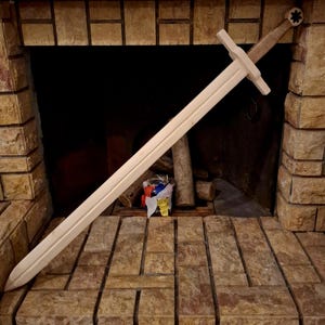 May include: A large, wooden sword with a cross-shaped hilt and a star-shaped pommel rests against a brick fireplace. The sword's blade is long and straight, and the handle is wrapped in a light-colored material. The sword is unpainted and appears to be made of unfinished wood.