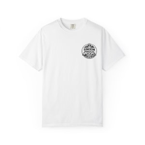 Puede incluir: Camiseta blanca de cuello redondo con un gráfico circular negro en el pecho izquierdo. El gráfico dice "UNION PROUD" y presenta una cordillera, una pancarta y otros elementos decorativos. La camiseta está hecha de un material suave.