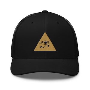 Può includere: Un cappellino trucker nero con un triangolo dorato ricamato sul pannello frontale. All'interno del triangolo si trova il simbolo nero dell'Occhio di Horus. Il cappellino presenta una parte anteriore strutturata, una visiera curva e una rete.