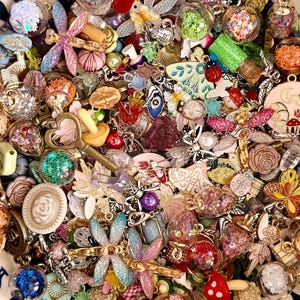 May include: A collection of colorful charms and pendants, including butterflies, dragonflies, mushrooms, and floral designs. The assortment features various colors, textures, and materials, such as glitter, beads, and metal. The charms are ideal for jewelry making or crafting.