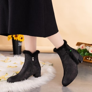 Peut inclure: Bottines noires avec un motif floral ton sur ton discret, une fermeture &eacute;clair lat&eacute;rale, un petit talon bloc et une bordure en fausse fourrure noire sur le haut. Un petit n&oelig;ud d&eacute;coratif avec une perle verte orne le c&ocirc;t&eacute; ext&eacute;rieur.