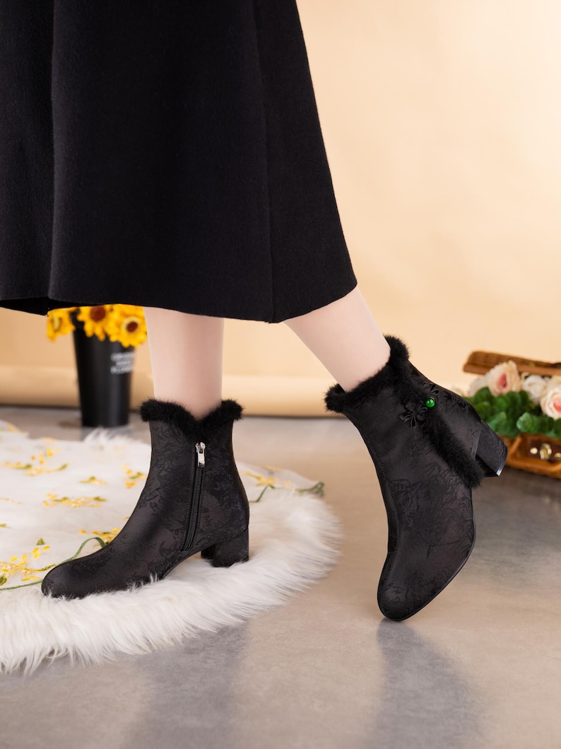 Peut inclure: Bottines noires avec un motif floral ton sur ton discret, une fermeture &eacute;clair lat&eacute;rale, un petit talon bloc et une bordure en fausse fourrure noire sur le haut. Un petit n&oelig;ud d&eacute;coratif avec une perle verte orne le c&ocirc;t&eacute; ext&eacute;rieur.