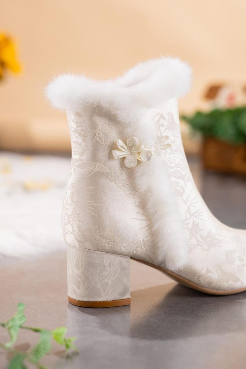 Peut inclure: Une bottine blanc cass&eacute; avec un motif floral ton sur ton subtil, une bordure &eacute;paisse en fausse fourrure blanche le long du col et de la couture lat&eacute;rale, et une fermeture d&eacute;corative en tissu en forme de fleur. Talon bloc et finition lisse.