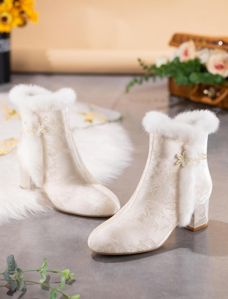 Peut inclure: Une paire de bottines couleur cr&egrave;me avec un motif floral jacquard subtil, une bordure en fausse fourrure blanche autour de l'ouverture sup&eacute;rieure et une fleur d&eacute;corative sur le c&ocirc;t&eacute;. Les bottines ont un talon bloc et un bout arrondi.