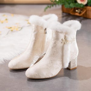 Peut inclure: Une paire de bottines couleur cr&egrave;me avec un motif floral ton sur ton discret, une bordure en fausse fourrure blanche au col, une fermeture &eacute;clair lat&eacute;rale et un bouton d&eacute;coratif en forme de fleur sur le c&ocirc;t&eacute; ext&eacute;rieur, sur un talon bloc.