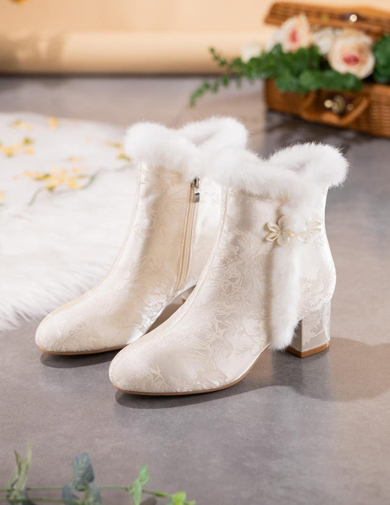 Peut inclure: Une paire de bottines couleur cr&egrave;me avec un motif floral ton sur ton discret, une bordure en fausse fourrure blanche au col, une fermeture &eacute;clair lat&eacute;rale et un bouton d&eacute;coratif en forme de fleur sur le c&ocirc;t&eacute; ext&eacute;rieur, sur un talon bloc.
