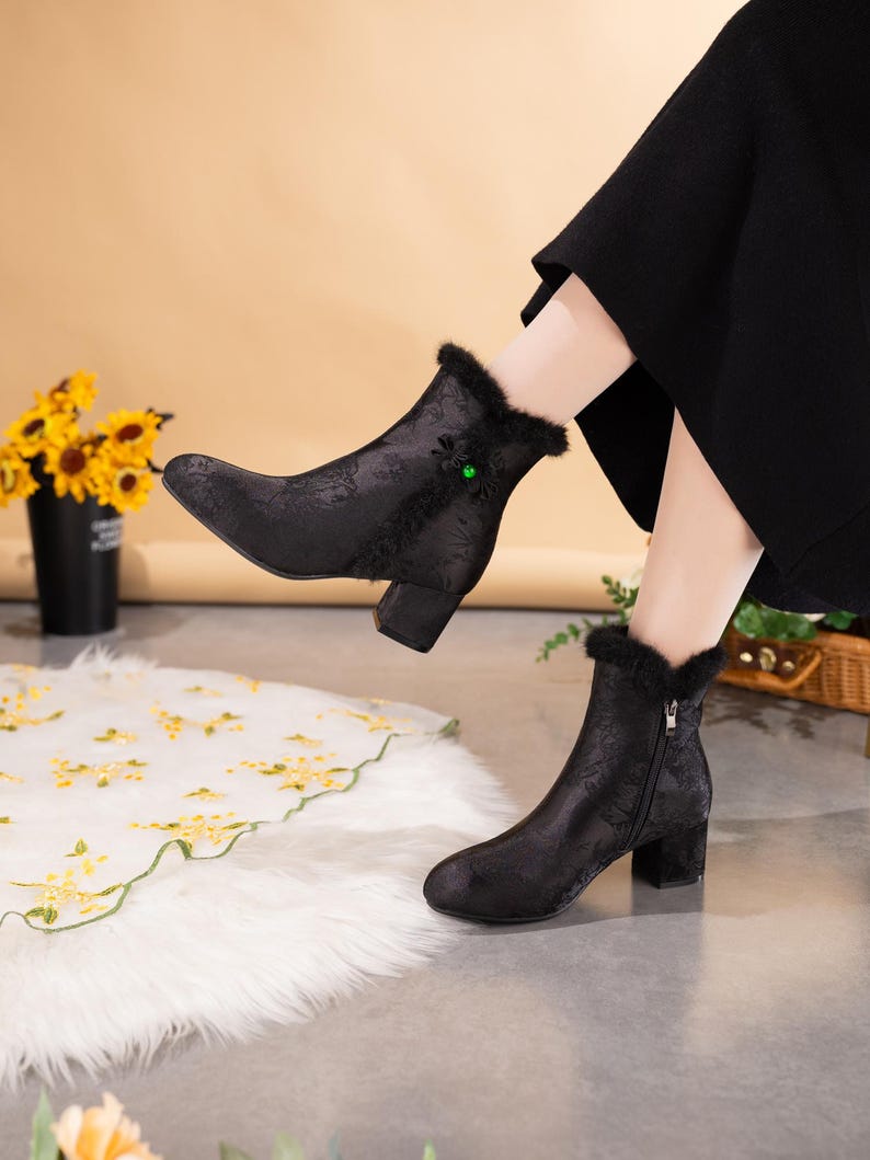 Peut inclure: Une paire de bottines noires avec un motif floral ton sur ton discret, un talon bloc et une bordure en fausse fourrure noire au niveau du col. Les bottines pr&eacute;sentent une fermeture &eacute;clair lat&eacute;rale et un petit bijou vert d&eacute;coratif sur le c&ocirc;t&eacute;.