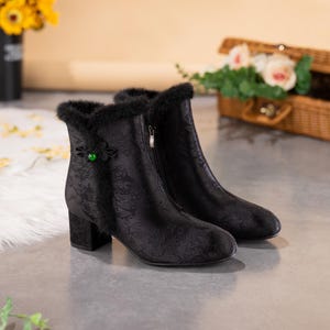 Peut inclure: Une paire de bottines noires avec un motif floral ton sur ton discret, une bordure en fausse fourrure noire sur le haut, une fermeture &eacute;clair lat&eacute;rale et un talon bloc. Un n&oelig;ud d&eacute;coratif en tissu noir avec une perle verte orne le c&ocirc;t&eacute;.