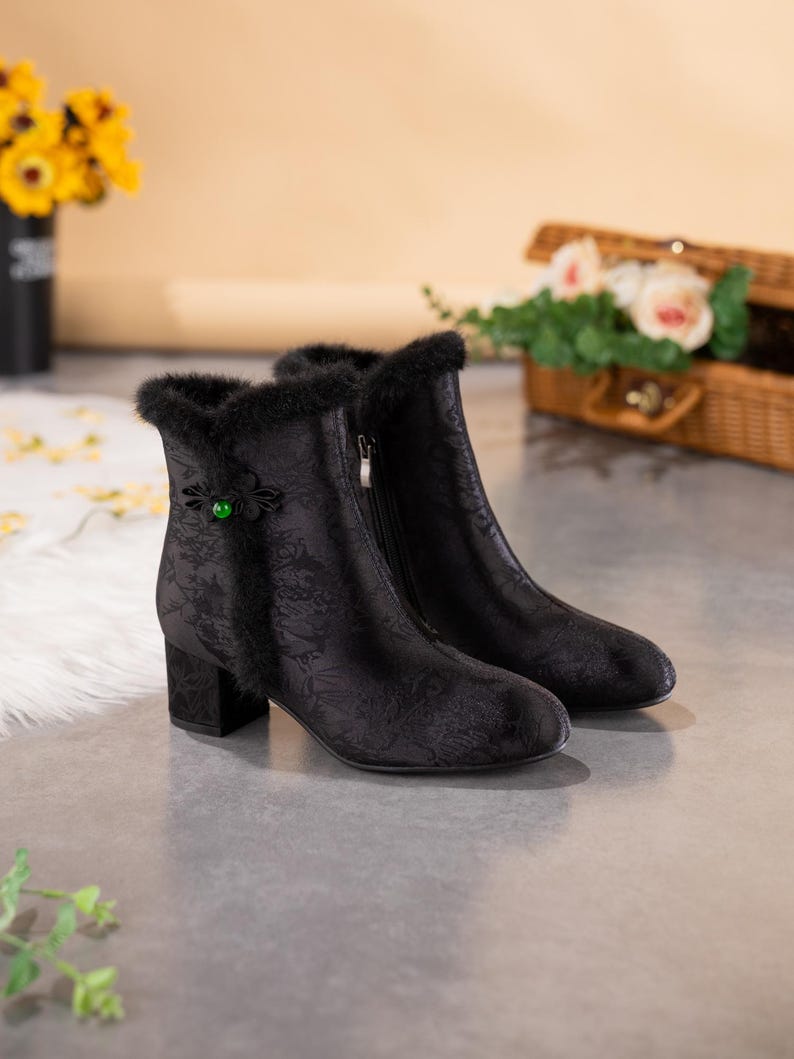 Peut inclure: Une paire de bottines noires avec un motif floral ton sur ton discret, une bordure en fausse fourrure noire sur le haut, une fermeture &eacute;clair lat&eacute;rale et un talon bloc. Un n&oelig;ud d&eacute;coratif en tissu noir avec une perle verte orne le c&ocirc;t&eacute;.
