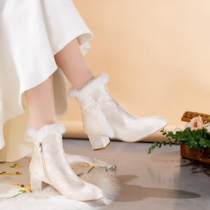 Peut inclure: Une paire de bottines couleur cr&egrave;me avec un motif floral subtil, un talon bloc et une bordure en fausse fourrure blanche au niveau du col. Les bottines comprennent une fermeture &eacute;clair lat&eacute;rale et un petit d&eacute;tail floral d&eacute;coratif sur le haut.