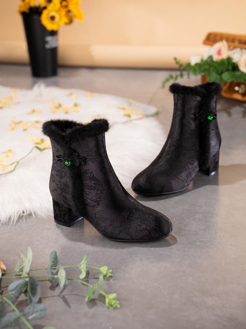 Peut inclure: Une paire de bottines noires avec un motif floral jacquard subtil, une bordure en fausse fourrure noire le long de l'ouverture sup&eacute;rieure et une perle verte unique sur la fermeture lat&eacute;rale. Les bottines ont un bout rond et un talon bloc.