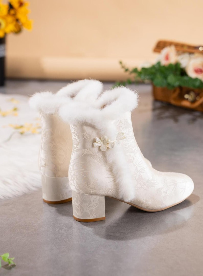 Peut inclure: Une paire de bottines blanc cass&eacute; avec un motif botanique ton sur ton subtil, une bordure &eacute;paisse en fausse fourrure blanche autour du col et de la couture lat&eacute;rale, et une petite d&eacute;coration florale blanche sur le c&ocirc;t&eacute;. Talon bloc et bout rond.