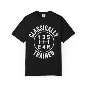 May include: Black t-shirt featuring the text "CLASSICALLY TRAINED" in white, encircling a white graphic of a manual transmission gear shift pattern. The shirt has a crew neck and short sleeves.
