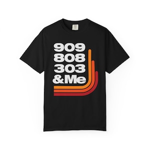 May include: Black t-shirt with the text "909 808 303 & Me" in white, accompanied by orange, red, and yellow curved lines. The shirt is a classic crew neck style.
