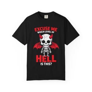 Puede incluir: Camiseta negra con un diseño de esqueleto con cuernos y alas rojas. El texto "EXCUSE ME WHICH LEVEL OF HELL IS THIS?" está en rojo y blanco. El diseño está centrado en la parte delantera.