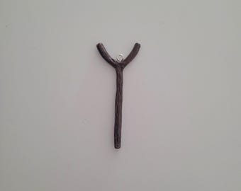 May include: A dark brown, Y-shaped pendant with a textured surface. The pendant has a small silver-coloured loop at the top for hanging. The pendant is set against a plain, off-white background.