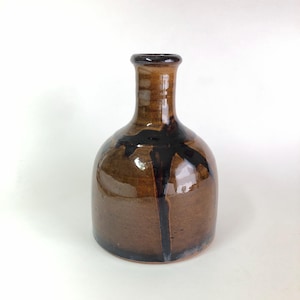 May include: A small, brown ceramic vase with a narrow neck and a wide, rounded base. The vase has a black glaze that runs down the side, creating a unique design.