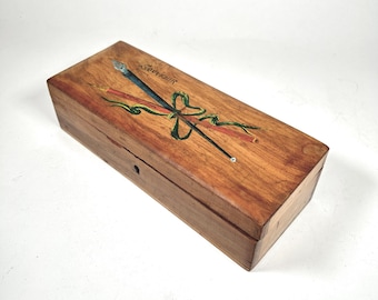 Caja antigua para lápices/plumas con decoración de recuerdo y pluma de caligrafía en la parte superior.
