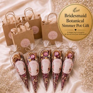 May include: Three brown paper gift bags with handles and round labels reading To My Bridesmaid, accompanied by five clear cone-shaped bags filled with dried flowers, orange slices, and cinnamon sticks, each featuring a floral label.