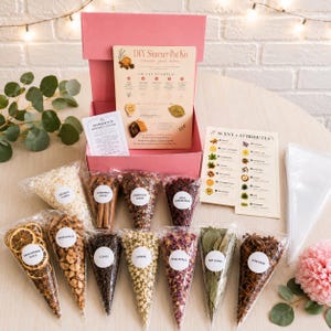 May include: A DIY simmer pot kit in a pink box containing various dried ingredients in clear cone-shaped bags, including orange slices, apple pieces, cloves, jasmine, rose petals, bay leaves, star anise, cranberries, and coconut flakes.